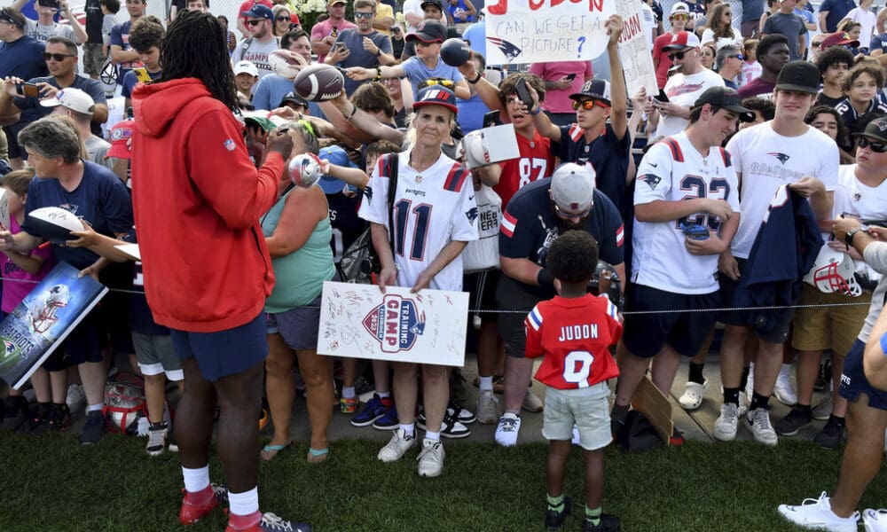 Chase Judon, 4, right, son of New England Patriots linebacker Matthew Judon, left, gives autographs with his father at the end of an NFL football practice, Sunday, July 30, 2023, in Foxborough, Mass. (AP Photo/Mark Stockwell)